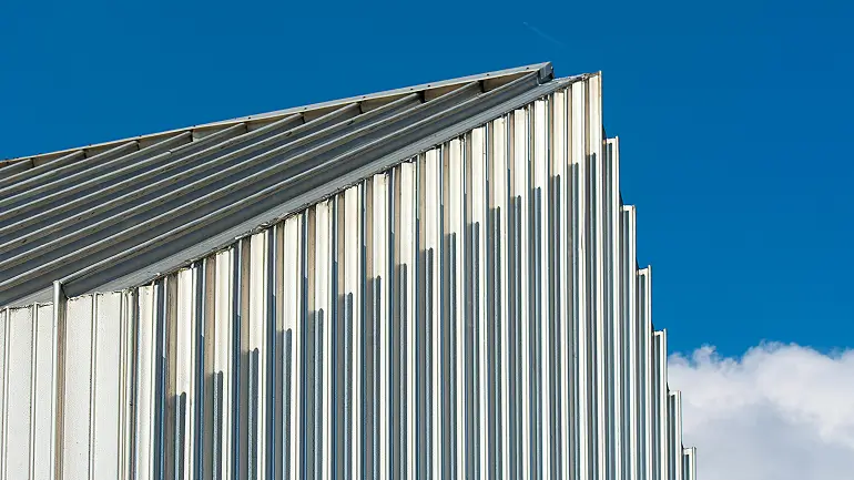 Close-up of a metal building wall with vertical ridges under a blue sky.