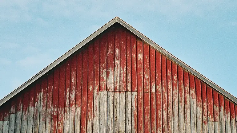 Top portion of a weathered red wooden barn under a partly cloudy sky.