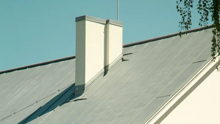 Close-up of a white chimney on a metal sloped roof under a clear blue sky.