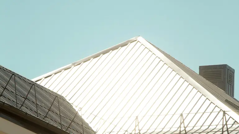 Close-up of sunlit white metal roof and dark roof side against a clear blue sky.