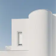 Minimalist white building with curved and straight sections under a clear blue sky.
