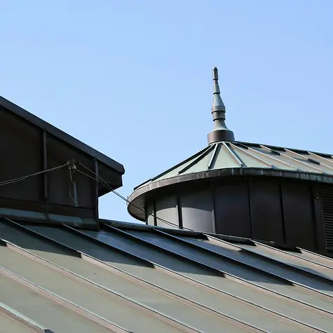 Close-up of metal building roofs with a pointed architectural finial under a clear blue sky.