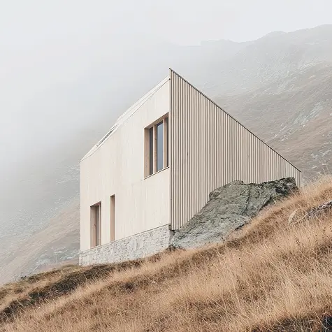 Modern house with beige wood siding on a rocky hillside with misty mountains in the background.